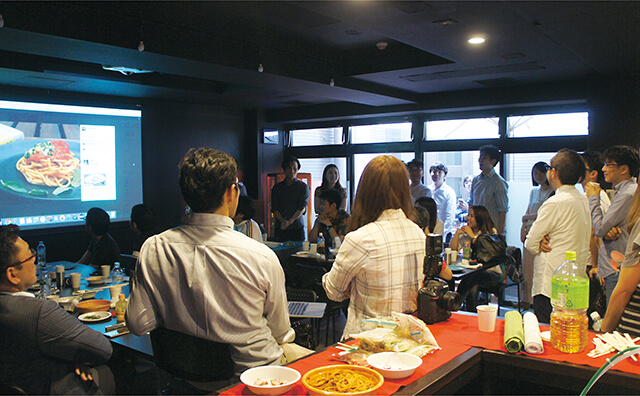 越後屋 高田馬場 Bスタジオの壁に設置されたスクリーンには料理写真が映し出され、HIUインスタ部で議論中